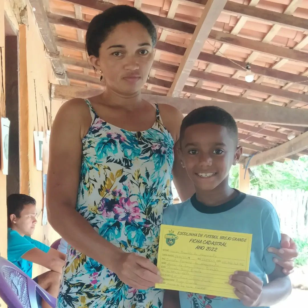 Na - imagem - uma - criança- ao - lado - do – mãe - exibindo - com - orgulho - a - ficha - de inscrição - da - Escolhia - de - Futebol – do - Brejo - Grande 